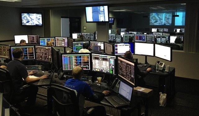IT professionals managing and monitoring systems in a control room with multiple screens