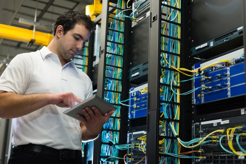 Network engineer using a tablet to monitor and manage server racks and structured cabling inside a modern data center